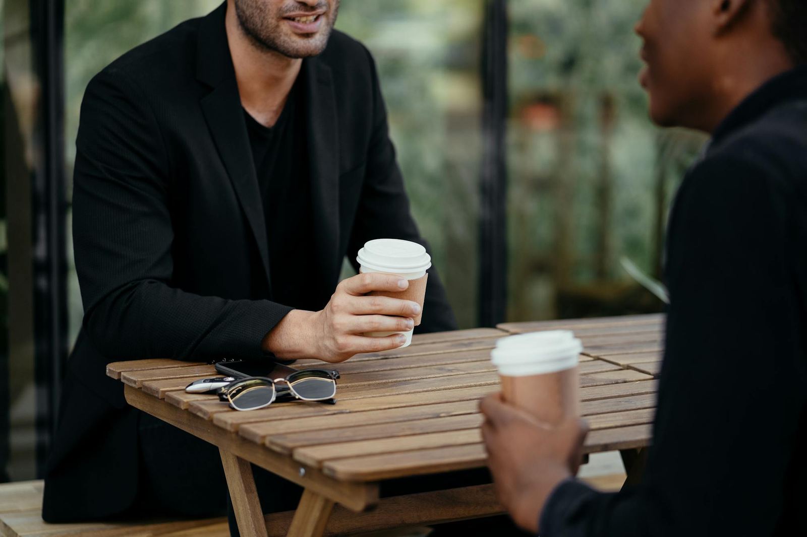 Two men talking over coffee outdoors in bright, warm daylight