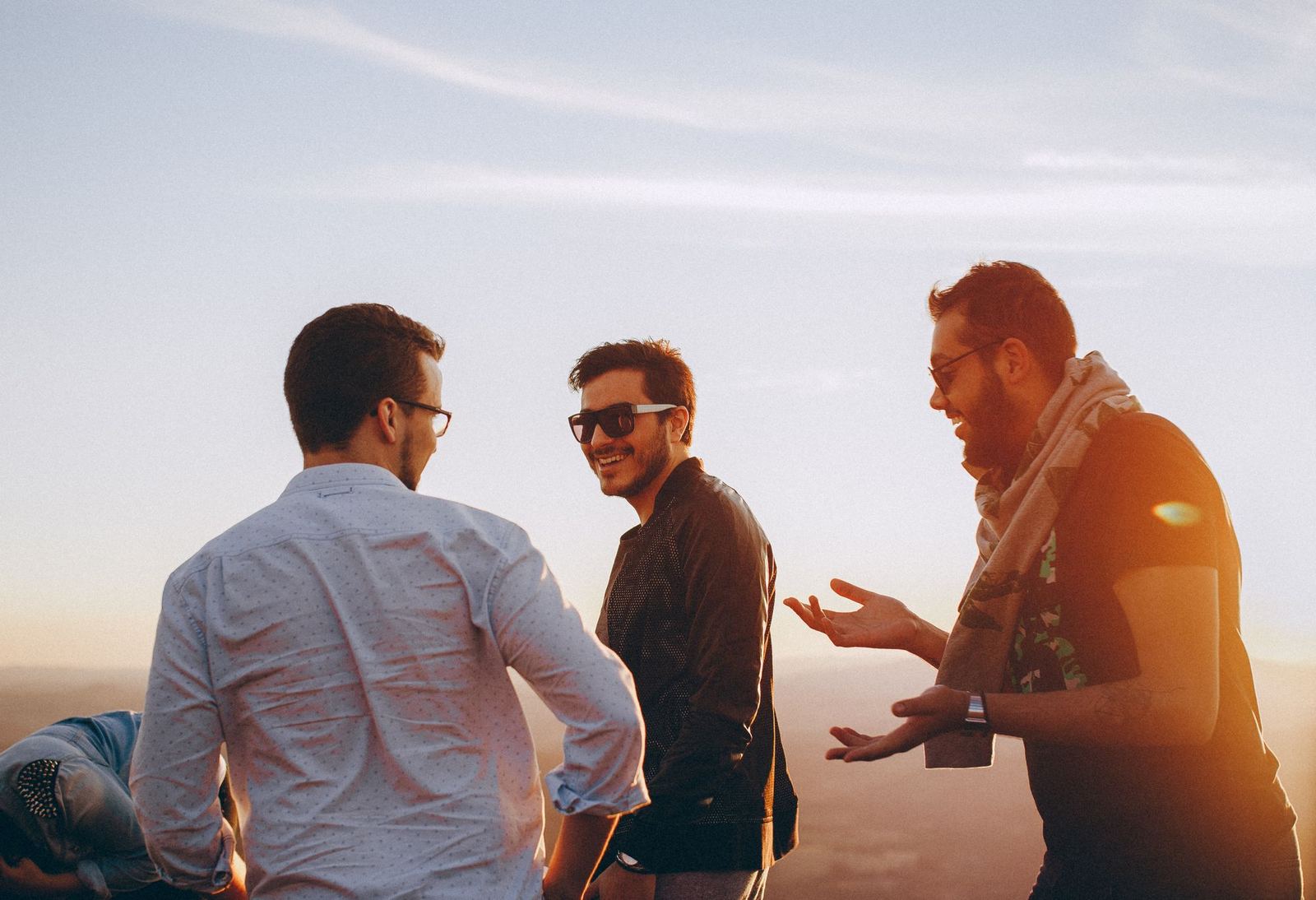 A small group of men laughing together outdoors in warm late-day light
