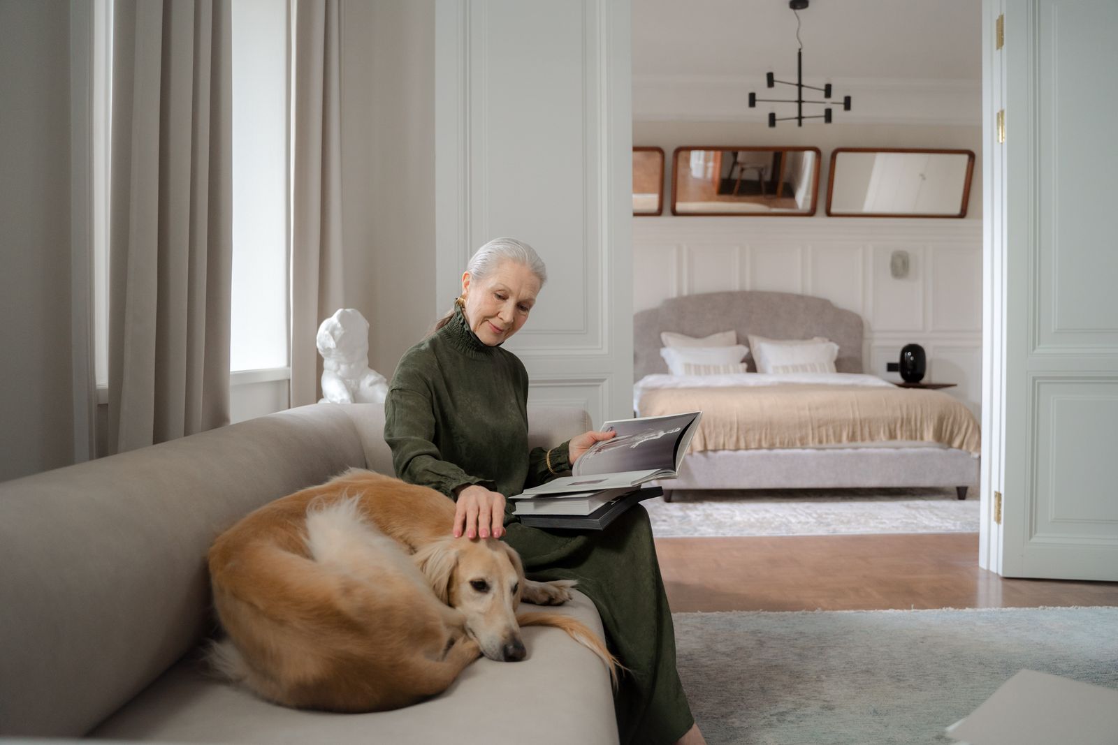 A silver-haired woman reading at home with her dog resting beside her