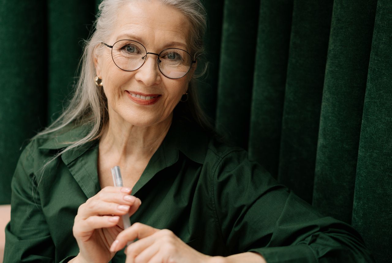 A silver-haired woman in round glasses with a warm, confident smile